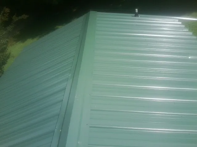 New green metal panels meeting at the ridge of a roof — Flat Roof Repair work by our crew in Moravia