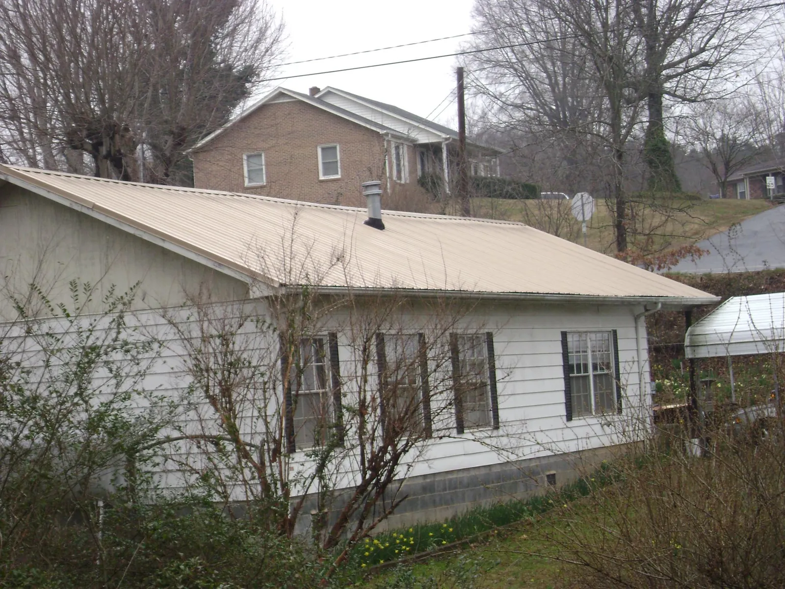 Tan metal roof on a white sided house set into a hillside — Commercial Roofing by Roofing Brothers in Moravia